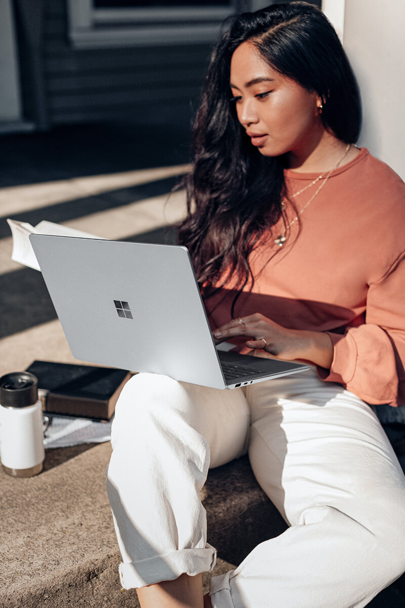 A girl sitting outside on a step with a Microsoft laptop.