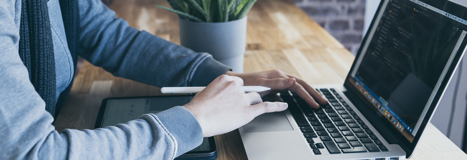 A person's hands using a Macbook laptop on a wooden table top.