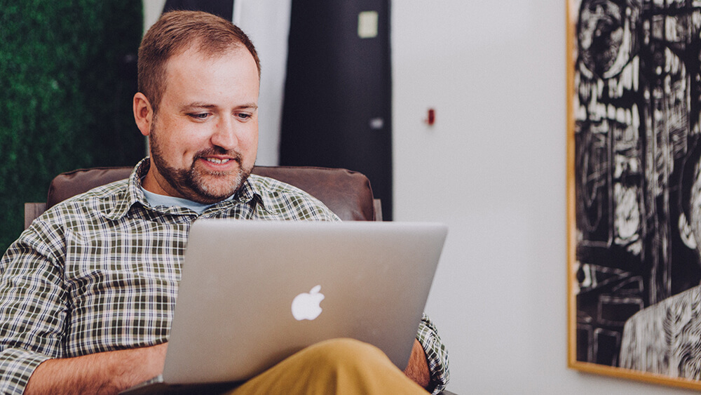 A smiling man on a laptop.